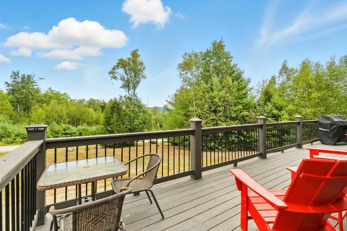 Een houten terras met een tafel en stoelen, omringd door een hekwerk en groen.