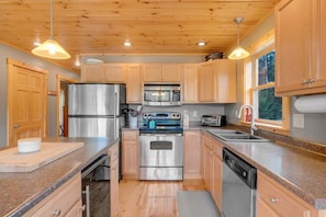 Una cocina moderna con armarios de madera, electrodomésticos de acero inoxidable, encimeras de granito e iluminación colgante.