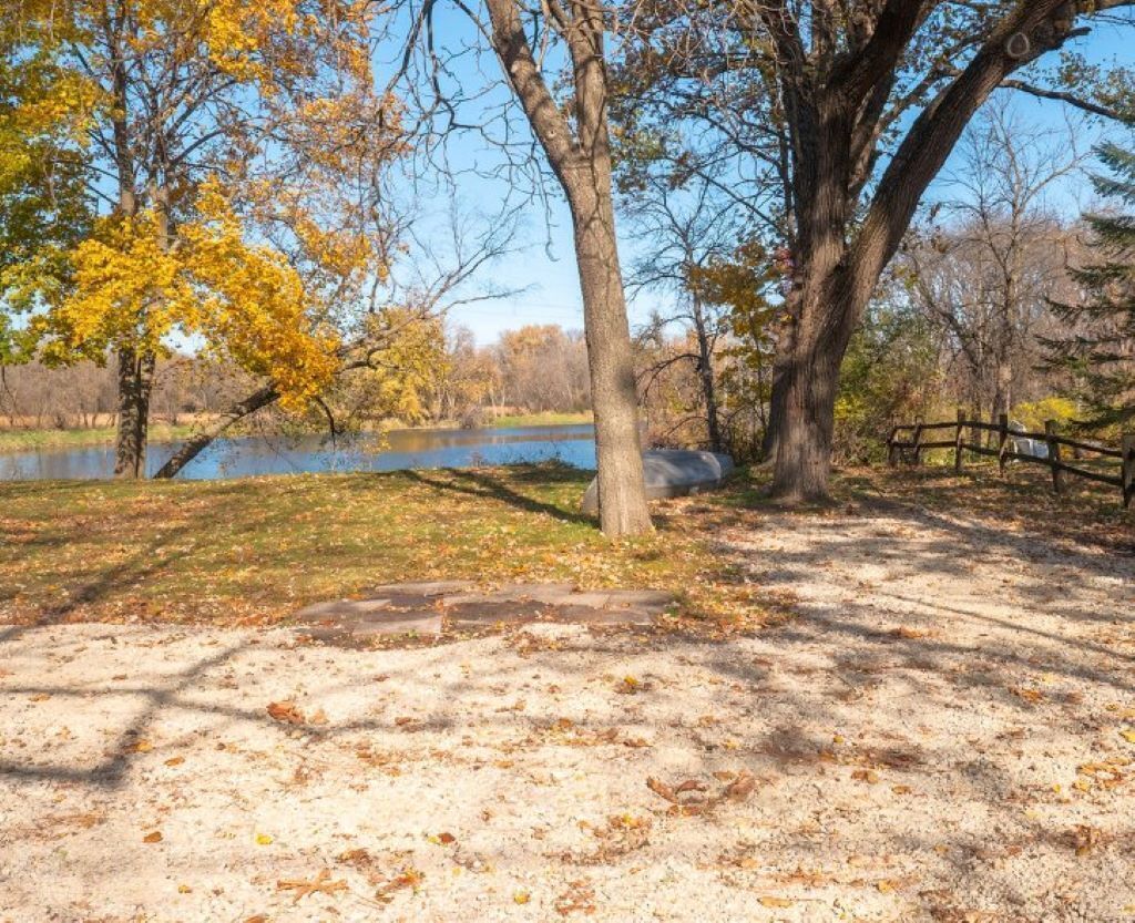 A park with trees, a lake, and a wooden fence.