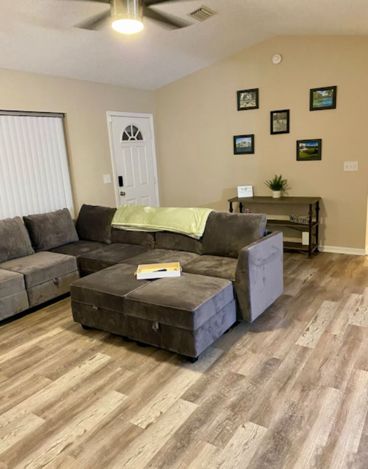A living room with a sectional sofa, ottoman, and a small table with a plant.