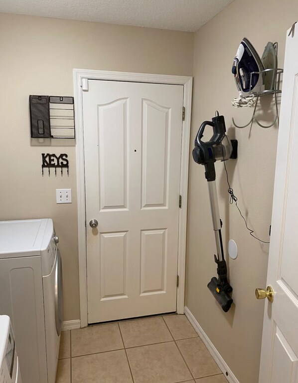 Une buanderie équipée d’un lave-linge, d’une porte et d’un aspirateur fixé au mur.