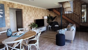 Una sala moderna con una mesa de comedor de madera, sillas blancas, un sofá y un televisor.