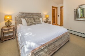 Un grand lit avec une tête de lit en bois, deux tables de chevet avec des lampes et un miroir au mur.