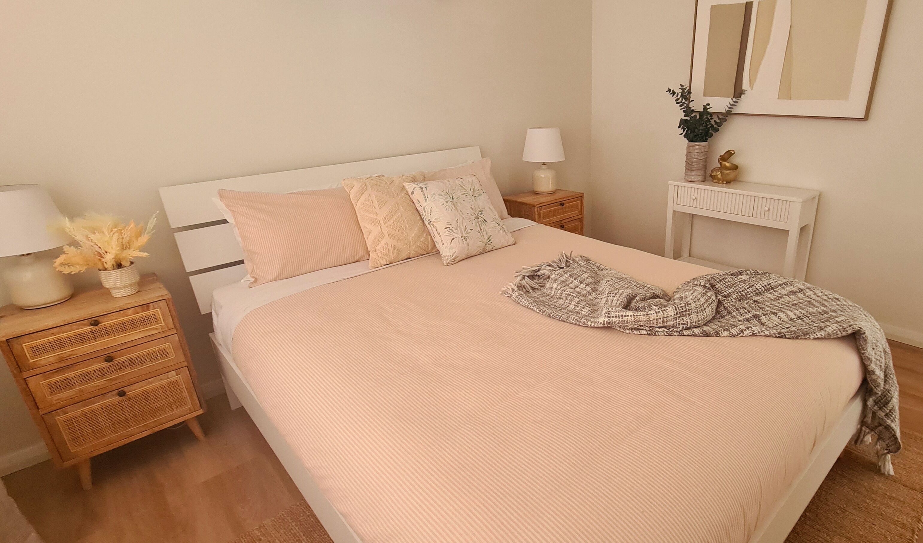 Un dormitorio ordenado con una cama grande, dos mesitas de noche, un tocador, un espejo y una planta pequeña.