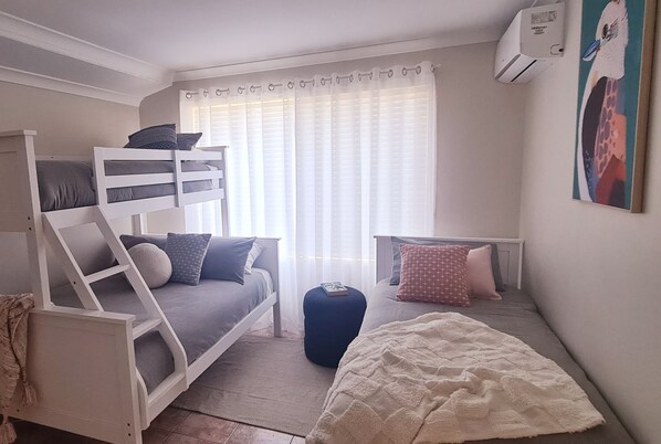 Een slaapkamer met stapelbedden, een klein bureau en een raam met dunne gordijnen.