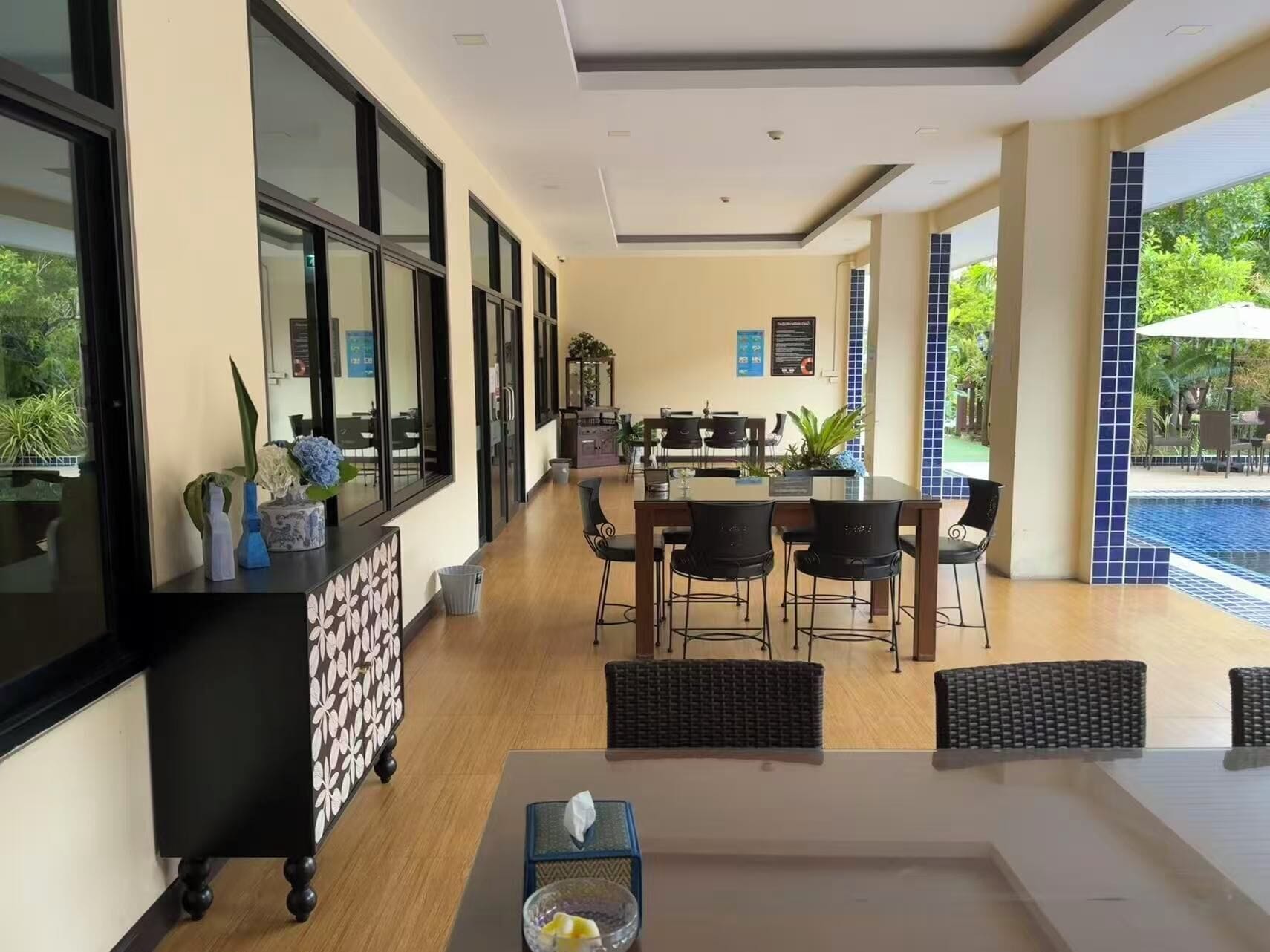 Un comedor moderno con vistas a la piscina, que incluye una mesa larga con sillas, una consola negra con objetos decorativos y un sofá de mimbre.