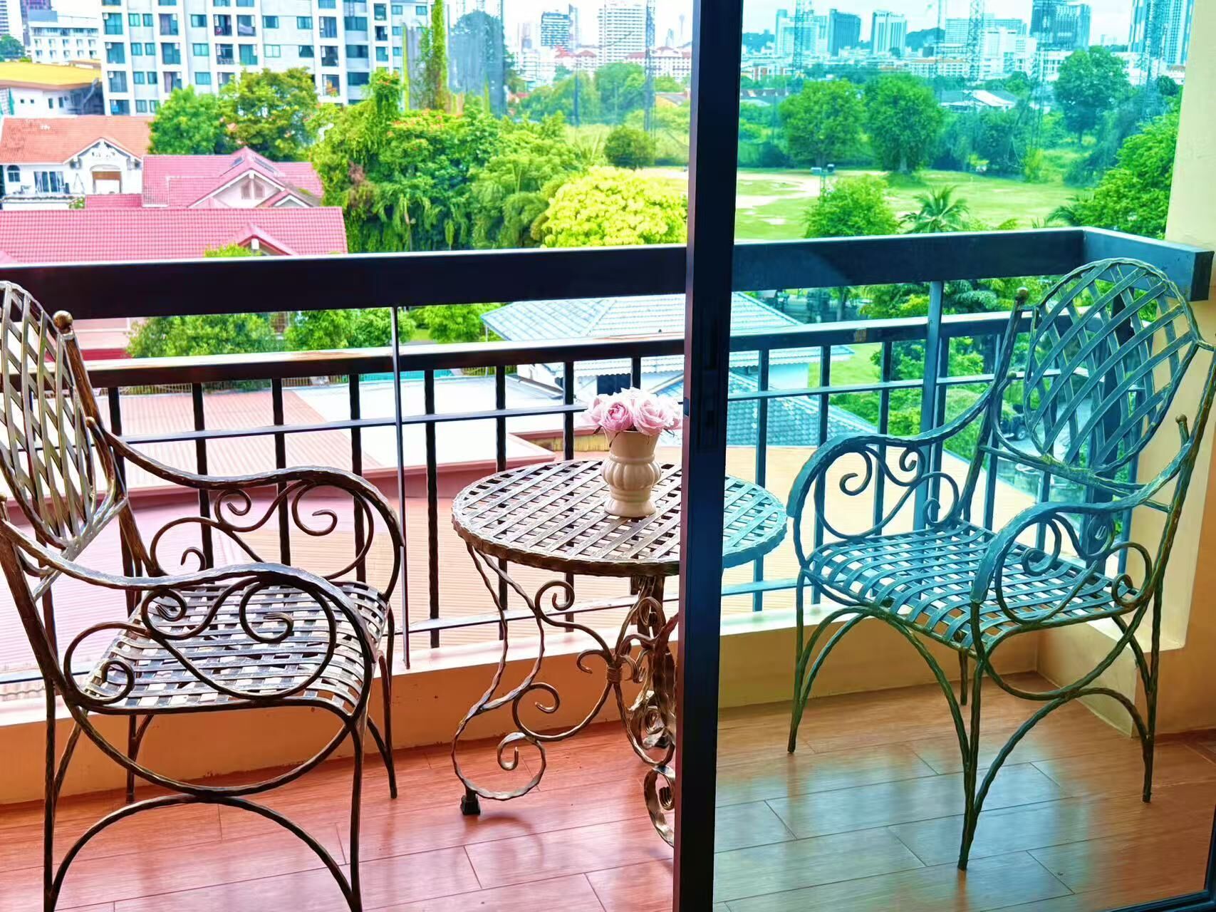 Un balcón con dos sillas y una mesa pequeña, con vista a un paisaje urbano con zonas verdes y edificios.