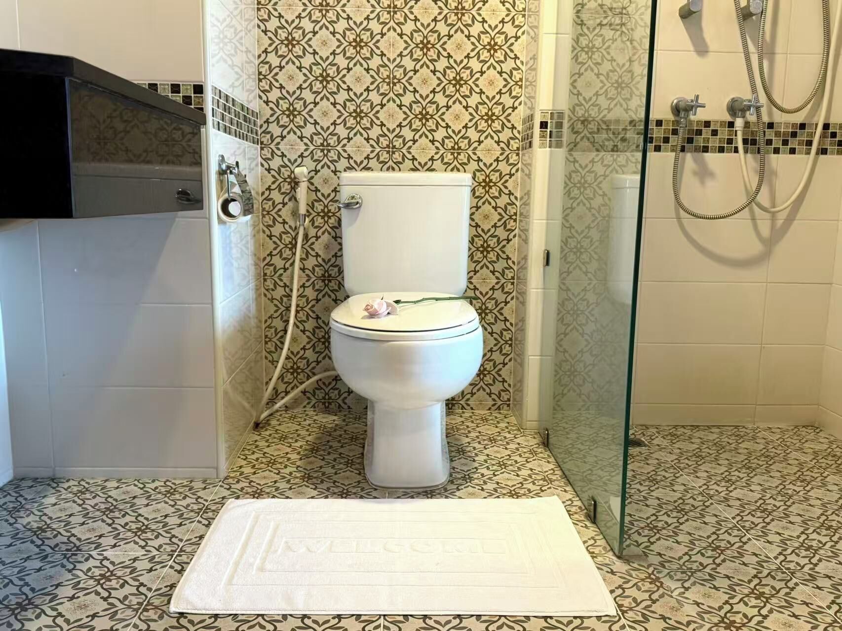 Un baño con inodoro, ducha y azulejos estampados.