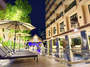 A poolside area with lounge chairs and umbrellas, a pool, and a building with balconies and windows. - MIDO HOTEL PATTAYA (Pattaya)