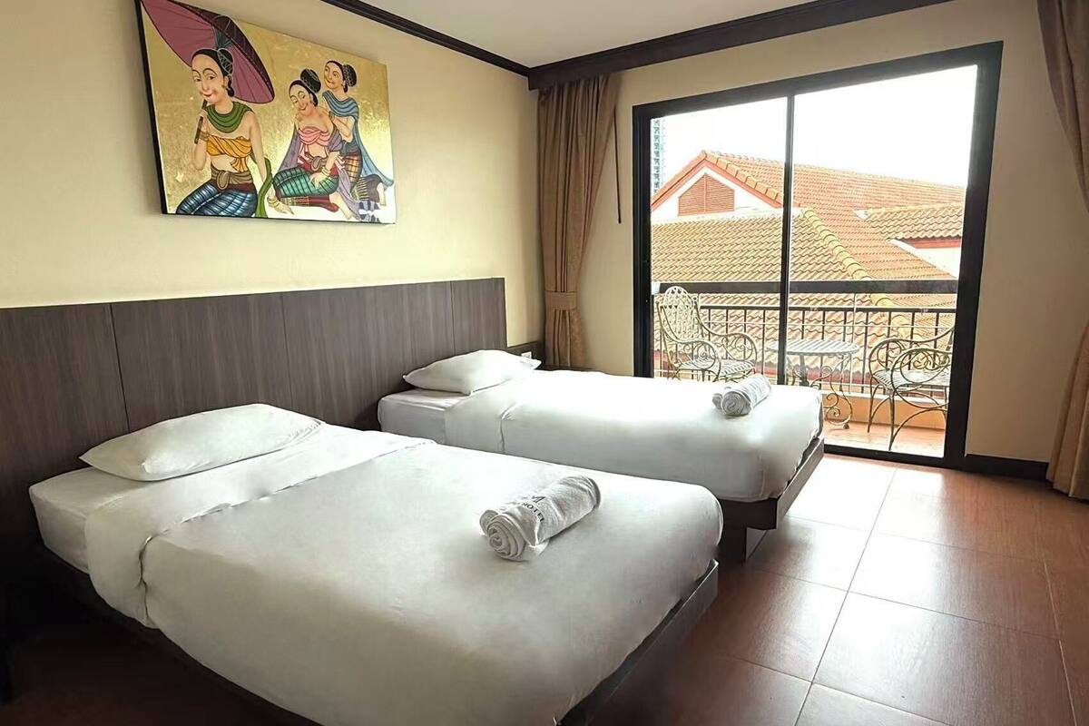 Habitación de hotel con dos camas, un balcón con vistas a edificios y un cuadro en la pared.