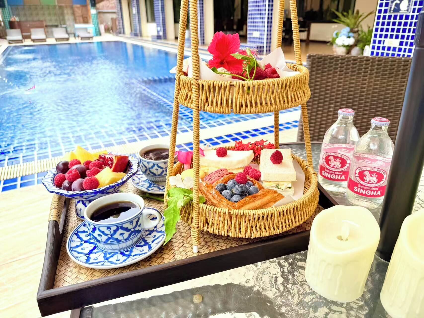 A breakfast tray with pastries, fruits, and beverages by a poolside.