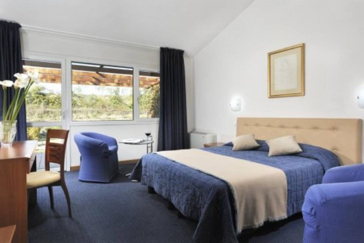 A hotel room with a bed, a desk, a chair, and a window with curtains.