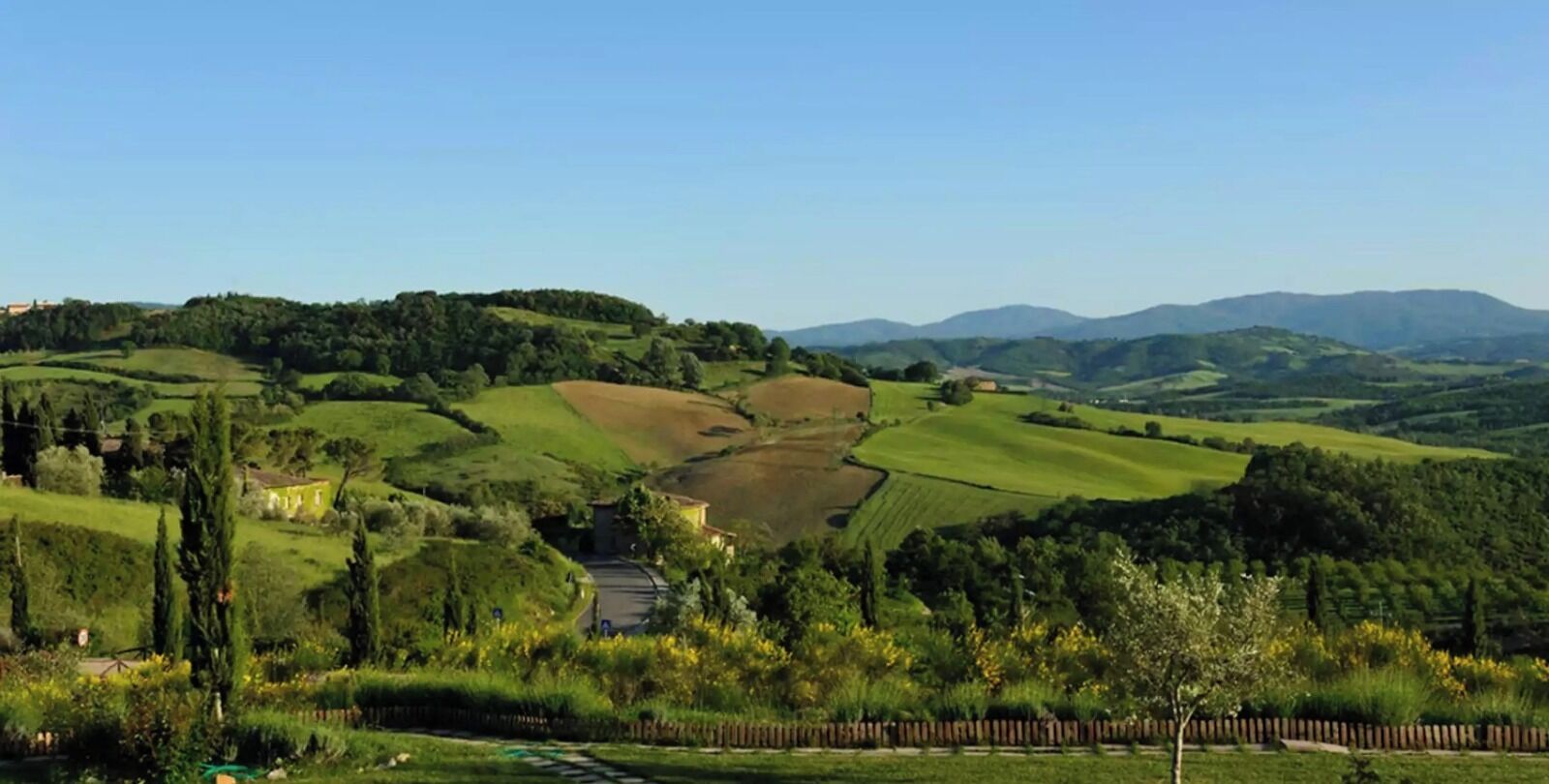 Ländliche Landschaft mit sanften Hügeln, einer kurvigen Straße und einem kleinen Gebäude im Vordergrund.