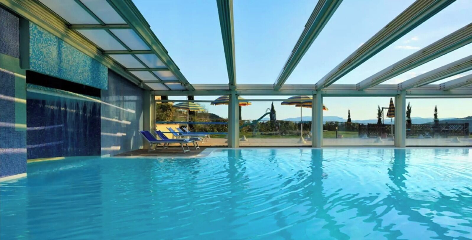 Une piscine à l’eau d’un bleu cristallin, entourée de murs de verre et de chaises longues bleues.