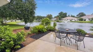 Une terrasse avec une table ronde et des chaises, un barbecue et un bassin orné d’une fontaine.