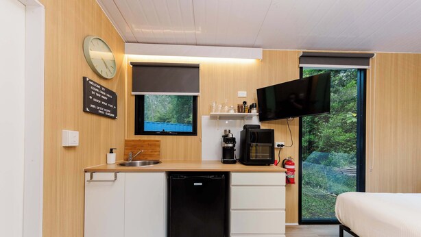 Cocina compacta con lavavajillas, cafetera y televisor montado sobre la encimera.