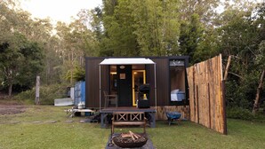 Una pequeña cabaña de madera con un porche, un brasero y un banco.