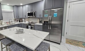 A modern kitchen with grey cabinets, a stainless steel refrigerator, a microwave, and a coffee station. -   House in Tampa fl  , 3-bedroom , 2 bathroom  , pool (Tampa)
