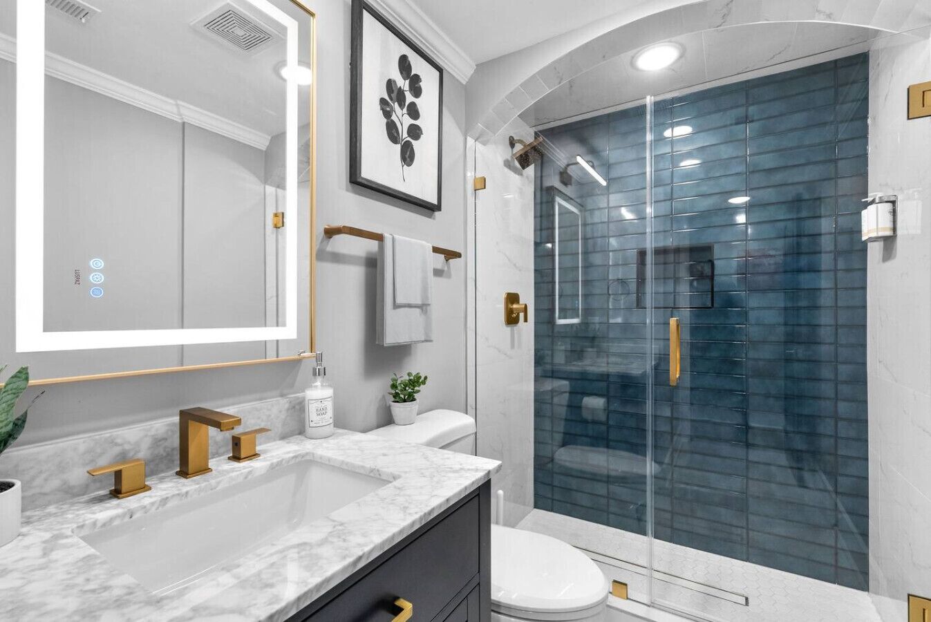 Un baño moderno con un espejo grande, lavamanos dobles, ducha con cerramiento de vidrio y encimera de mármol.