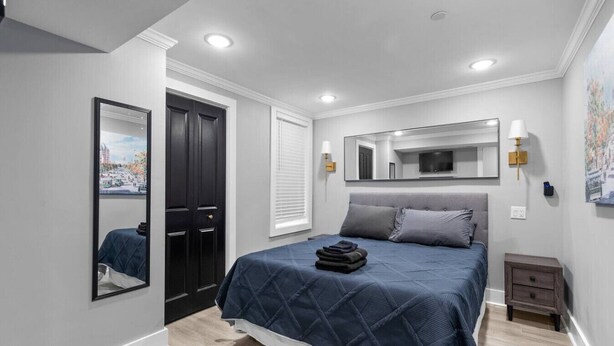 A modern bedroom with a bed, a large mirror, a nightstand, and a window with blinds. - DC Urban Retreat+3Bed+Newly Renovated (Washington)