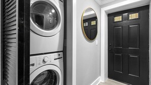 A laundry area with stacked washers and dryers, a black door with a gold handle, and a round mirror on the wall. - DC Urban Retreat+3Bed+Newly Renovated (Washington)