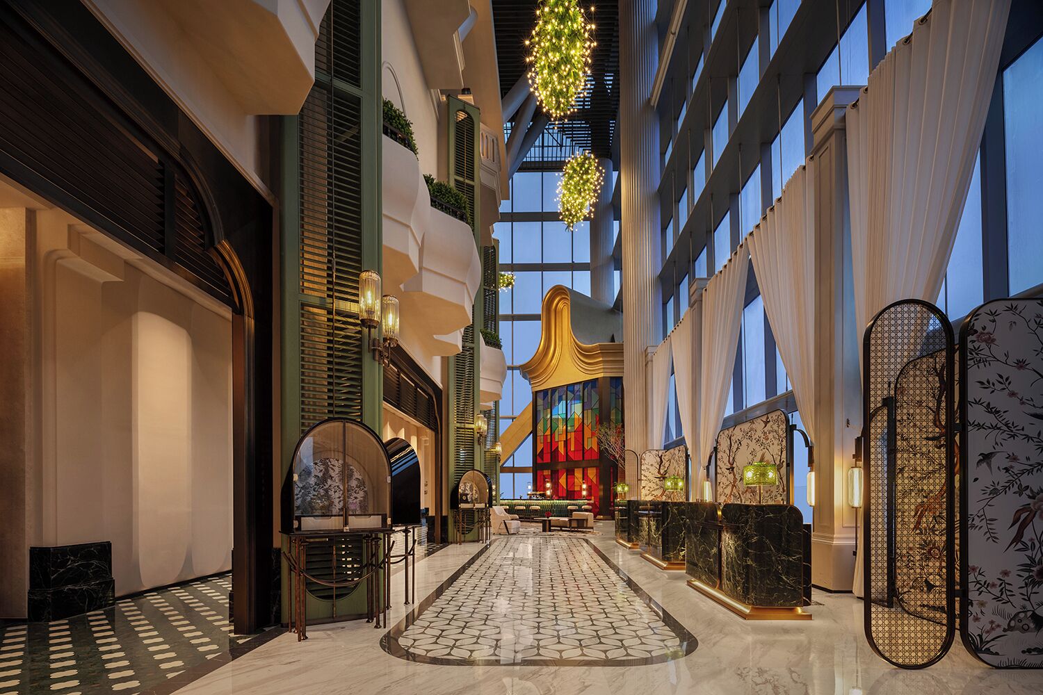 Un amplio vestíbulo de hotel con una zona de estar central, suelo estampado y ventanas grandes.