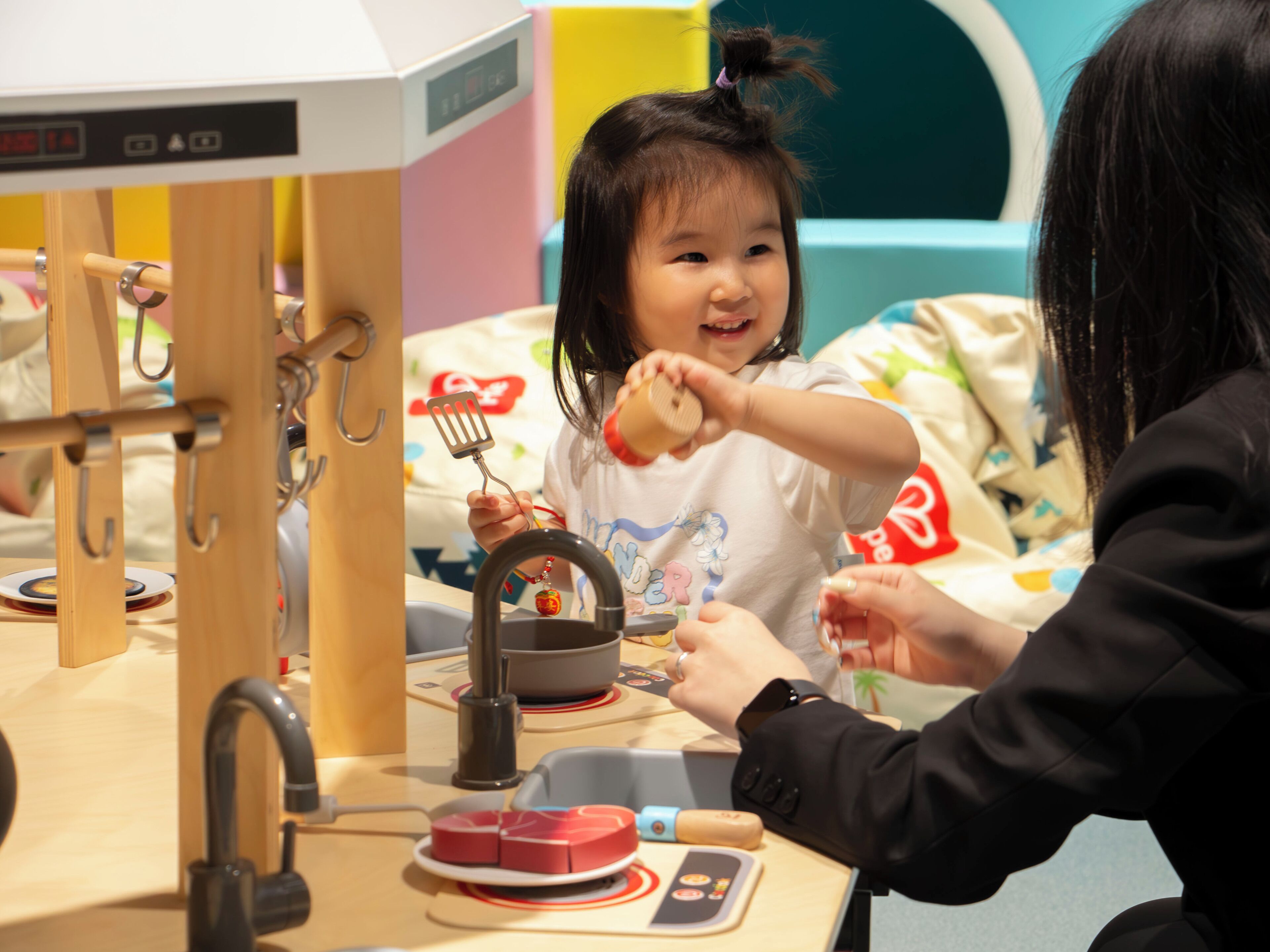 A child playing with a toy kitchen set, including a faucet and a bowl.