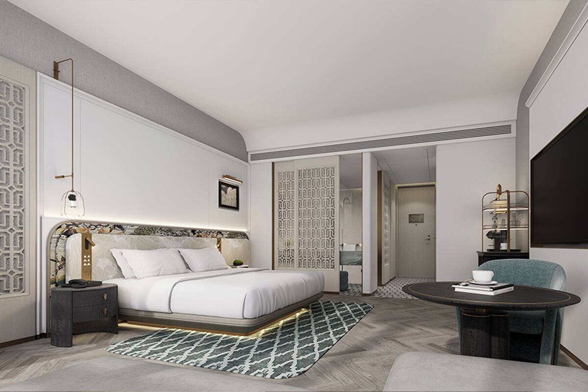 Ein modernes Hotelzimmer mit Bett, Nachttisch, Sessel und einem kleinen runden Tisch mit Tasse und Buch.