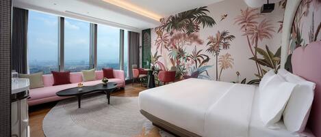 Habitación de hotel moderna con una cama grande, un sofá rosa, una mesa de centro redonda y vistas de la ciudad a través de amplios ventanales.