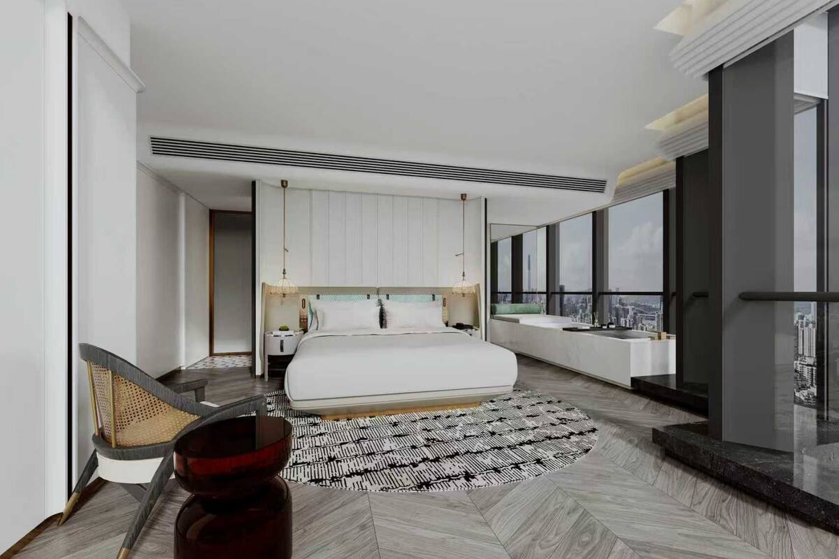 Ein modernes Schlafzimmer mit einem großen Bett, einer Sitzecke mit einem Sessel und Blick auf die Stadt durch große Fenster.