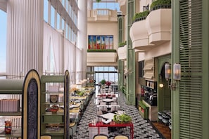 Un vestíbulo de hotel con varias zonas de restauración, una escalera central y vistas a la ciudad.