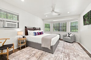 A bedroom with a bed, a chair, a desk, and a ceiling fan.