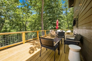 An outdoor deck with wooden flooring, a metal railing, and outdoor furniture including chairs and a table.