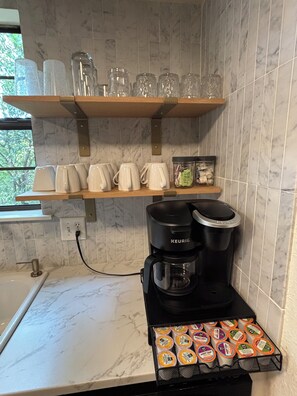 A kitchen with a Keurig coffee maker, a tray of coffee pods, and a shelf with mugs and a jar of creamer. - The Gravity Getaway, it's all downhill from here. (Bella Vista)