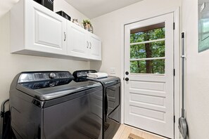 A laundry room with two front-loading washing machines, a white door with a window, and white cabinetry above.