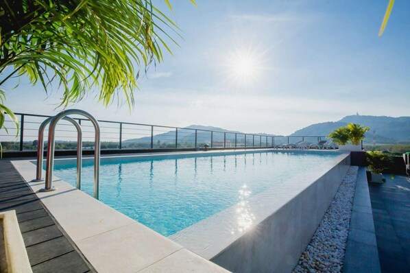 Une piscine avec un escalier en métal, entourée d’une terrasse dotée d’une rambarde, et offrant une vue sur les montagnes en arrière-plan.