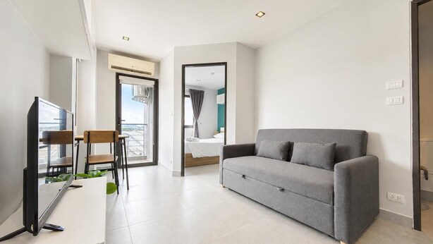 A modern hotel room with a grey sofa, a TV, and a dining area with chairs and a table.