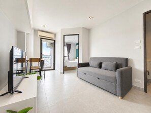 A modern hotel room with a grey sofa, a TV, and a dining area with chairs and a table. - Boutique Bliss 1BR T1-506 (Chalong)