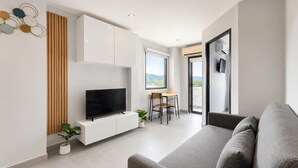 A modern living room with a flat-screen TV, a sofa, a dining area with a table and chairs, and a large window with a view.
