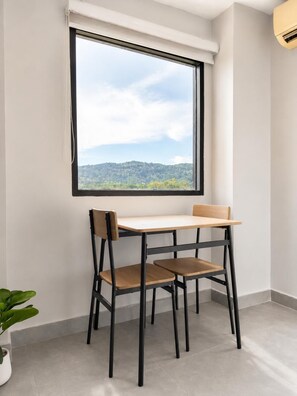 A corner room with a large window, a table, two chairs, and a potted plant. - Boutique Bliss 1BR T1-506 (Chalong)