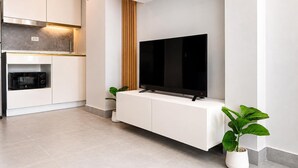 A modern kitchen with white cabinetry, a built-in microwave, and a flat-screen TV mounted on a white console.