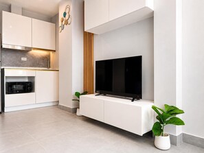 A modern kitchen with white cabinetry, a built-in microwave, and a flat-screen TV mounted on a white console. - Boutique Bliss 1BR T1-506 (Chalong)