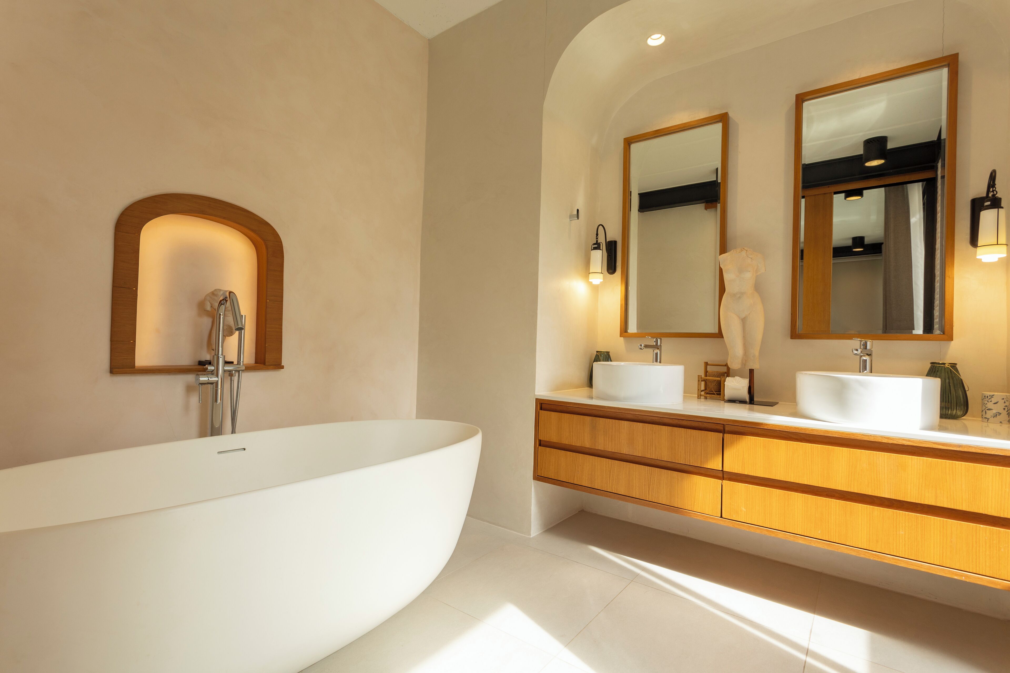 A modern bathroom with a freestanding bathtub, two sinks, wooden cabinetry, and wall-mounted mirrors.