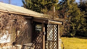 Una cabaña Pioneer con una puerta de celosía de madera, rodeada de árboles y un área verde.
