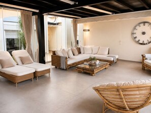 A modern living room with a sectional sofa, a rattan chair, and a large wall clock.
