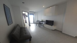 Een moderne woonkamer met een bank, een televisie en een eethoek met stoelen en een kleine tafel.