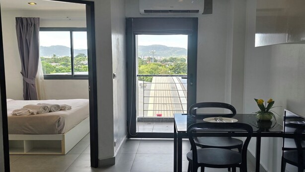 Een hotelkamer met een bed, een eettafel met stoelen en uitzicht op een balkon met stadsbeeld.