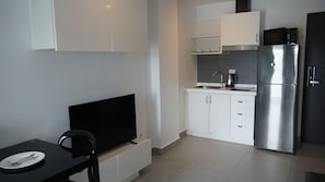 Eine moderne Küche mit weißen Schränken, einem Edelstahl-Kühlschrank, einer Mikrowelle und einem Flachbildfernseher auf einem schwarzen Lowboard.