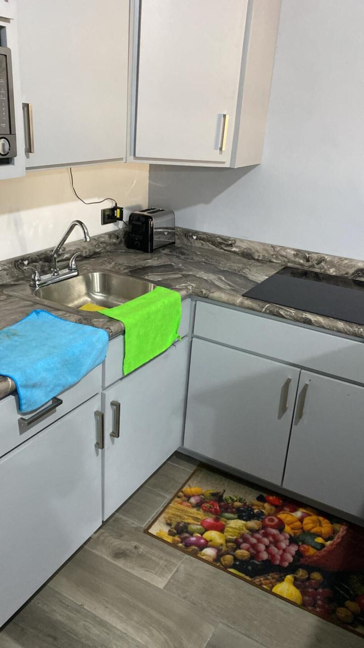 Una cocina con un lavabo, un tostador y un frutero en el suelo.
