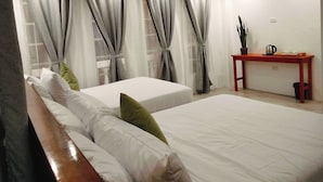 Une chambre d’hôtel avec deux lits, une tête de lit en bois, une petite table avec une plante et une fenêtre avec des rideaux.